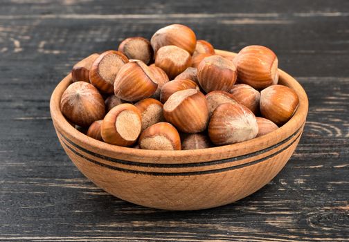 Full bowl of fresh hazelnuts in the shell on the wooden background