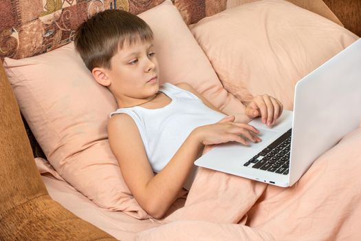 Young boy plays games on a laptop in bed