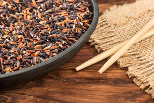 Part of frying pan with black wild rice and chopsticks on wooden background