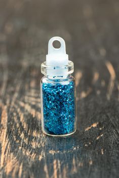 Blue glitter in a small bottle of make-up on wooden background