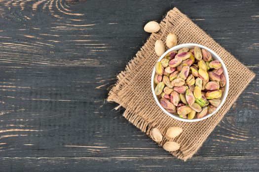 Pistachios in a bowl and scattered nuts on mashchvone and wooden background, top view