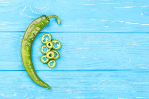 Fresh green chili pepper with slices on a blue wooden background, top view