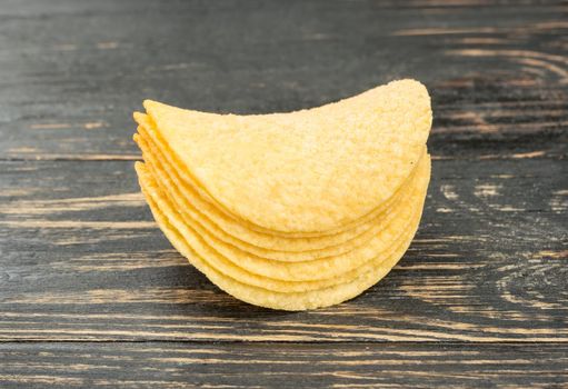 Small stack of potato chips on wooden background closeup