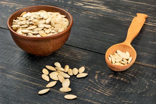 Pumpkin seeds in a shell in a spoon and a bowl on the table