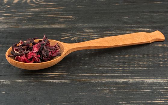 Dry karkade tea in a spoon on wooden background closeup