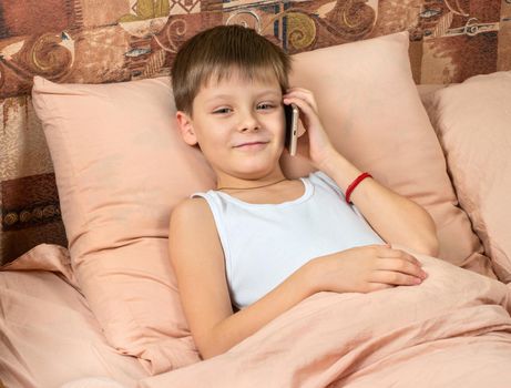 Happy young boy making phone calls in bed