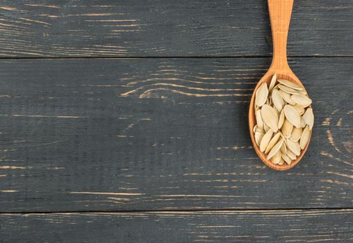 Pumpkin seeds in shell and spoon on empty wooden background