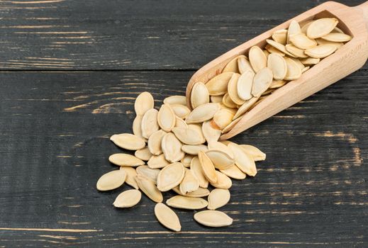 Pumpkin seeds in scoop on wooden background closeup