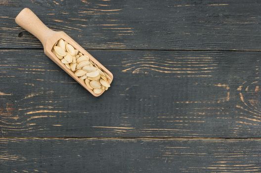 Pumpkin seeds in scoop on empty wooden background