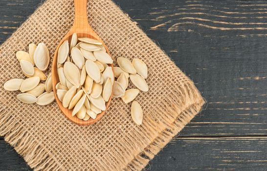 Pumpkin seeds in shell on burlap on wooden background closeup