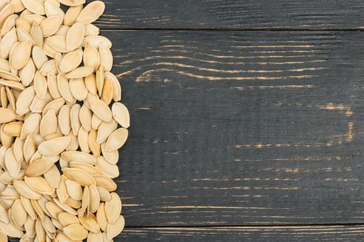 Scattered pumpkin seeds on an empty wooden background, top view