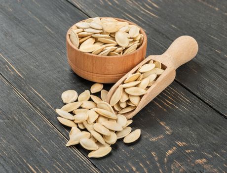 Pumpkin seeds in scoop and bowl on wooden background