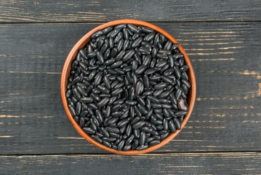 Bowl with black beans on a wooden background, top view