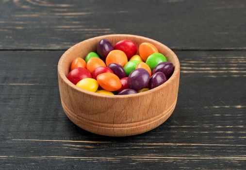 Multicolored candy in a bowl on a wooden background close-up