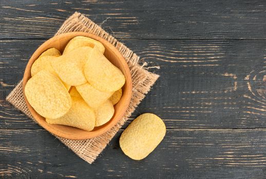 Bowl of potato chips on the empty burlap on wooden background