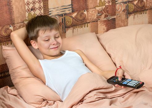 Young boy with remote control in hand watching TV in bed