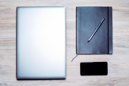 minimalist flat lay of a laptop, smart phone, notebook and pen on a wooden table, concept of online entrepreneur and remote work