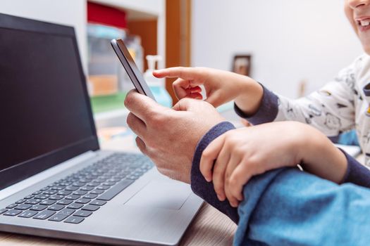 detail of a child hands bothering his father while working at home with his smartphone and computer, work at home concept due to the coronavirus pandemic