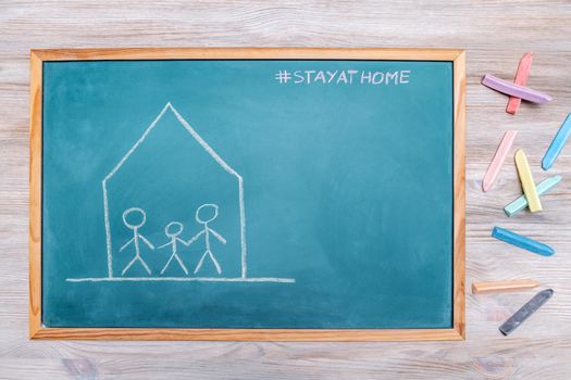 confined family drawn on a blackboard with the message stay at home and colored chalk next to it, concept of quarantine with children, copy space for text