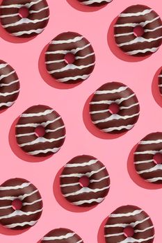 Concept food design with tasty chocolate glazed donut with white strips on coral pink pastel background top view pattern. Mock up, flat lay style