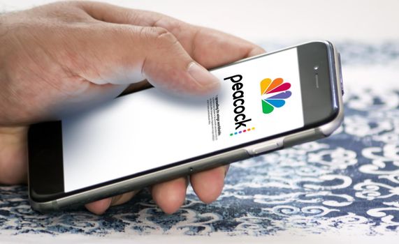 New York, USA, May 2022: hand holding a phone with the Peacock Tv mobile app on the screen. Peacock is an American video streaming service owned by NBCUniversal