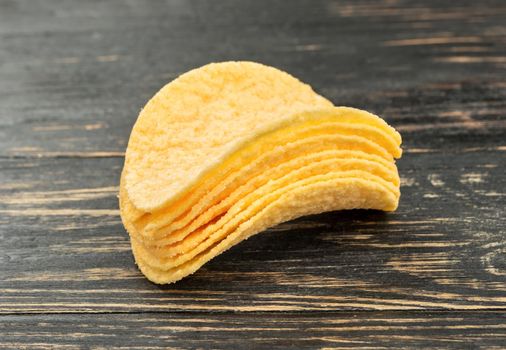 Small stack of potato chips on wooden background closeup