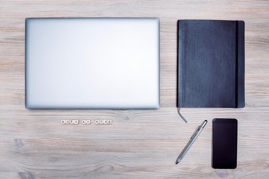minimalist flat lay of a computer, smart phone, notebook and pen on a wooden table with the message "work at home", concept of online entrepreneur and remote work