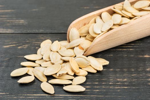 Pumpkin seeds in scoop on wooden background closeup