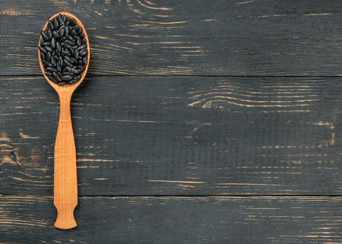 Black beans in wooden spoon on empty wooden background