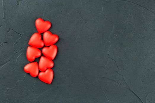 Scattered red plastic hearts on empty dark background, top view