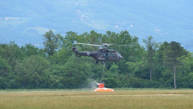 Cerklje Slovenia MAY 29, 2022 Fire helicopter fills the bambi bucket with water while hovering over a tank. Eurocopter AS532 Cougar, Airbus Helicopters H215M, of Slovenian Air Force. Copy space