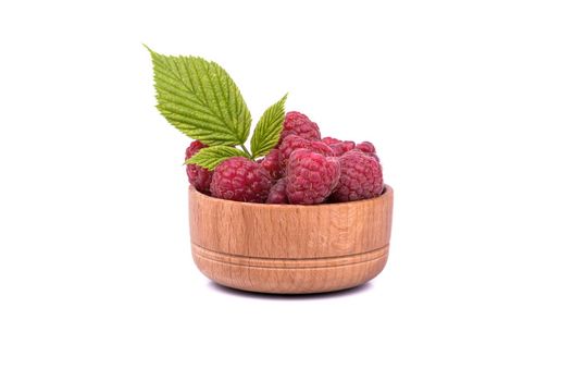 Full wooden bowl of fresh raspberries with leaves on a white background