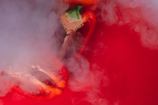 SWEET, fresh RED PEPPER ON A RED BACKGROUND, cut in half, thick smoke around. proper nutrition. fresh vegetables