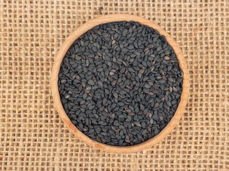 Black sesame seeds in a bowl on a burlap, top view