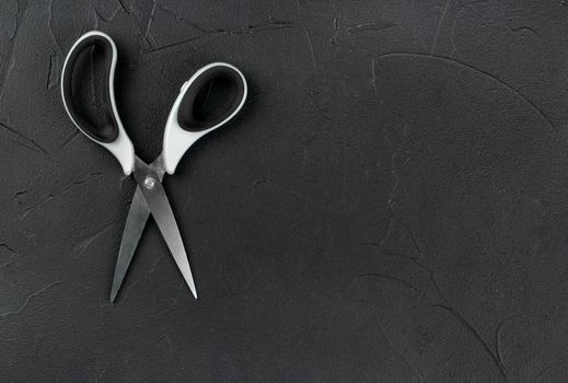 Scissors with plastic handle on empty dark background, top view