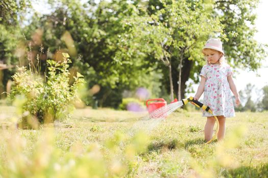 Adorable little girl playing with a garden hose on hot sunny summer day