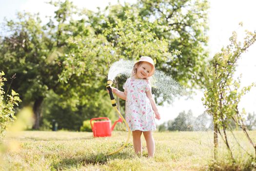 Adorable little girl playing with a garden hose on hot sunny summer day