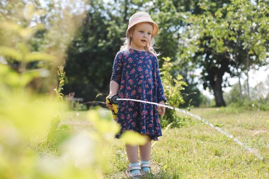 Adorable little girl playing with a garden hose on hot sunny summer day