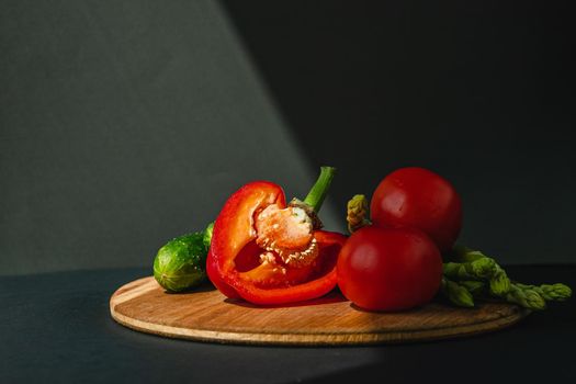 branches of fresh green asparagus, peppers, tomatoes and cucumbers on a wooden board, dark gray background, top view. Basic trend concept with copy space