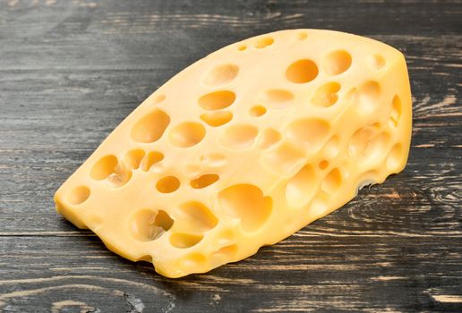 Piece of cheese with holes on dark table close up