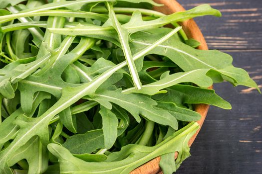 Green arugula leaves in a bowl on a dark table closeup