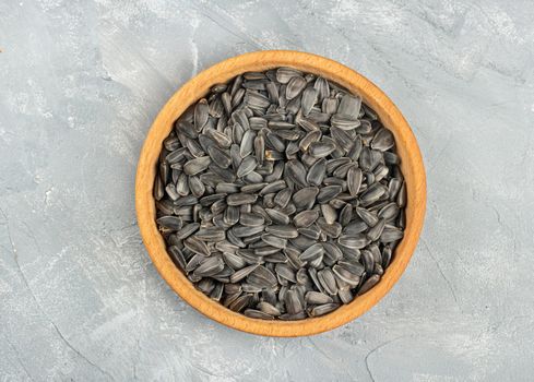 Large wooden bowl with sunflower seeds on concrete background, top view