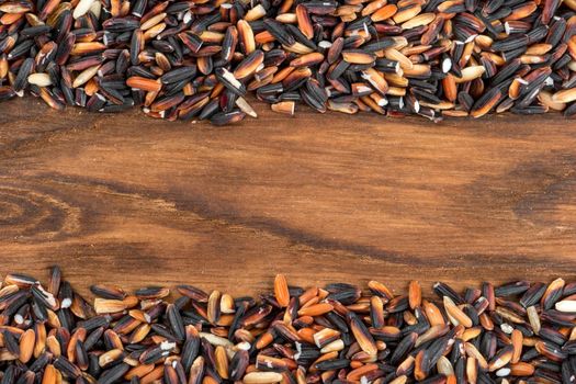 Frame of wild black rice in wooden background under the text