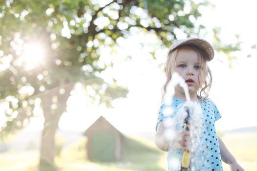 Adorable little girl playing with a garden hose on hot sunny summer day