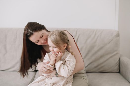 Cheerful toddler daughter and happy mother in a cozy light room at home. Mother's Day love family parenthood childhood concept