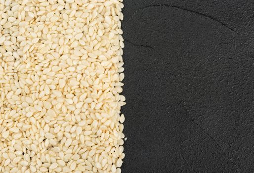 Scattered sesame seeds on a dark concrete background, top view