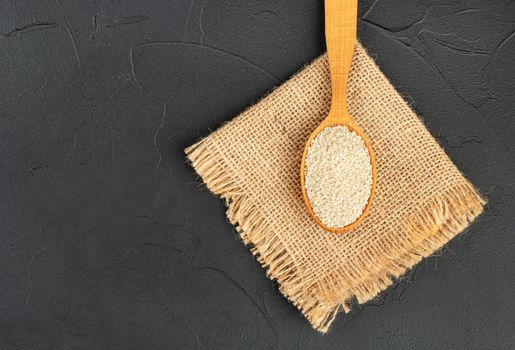 Sesame seeds in wooden spoon on burlap and dark background