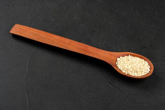 Small spoon with sesame seeds on dark background