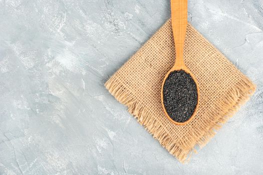 Black sesame in wooden spoon on burlap and light background
