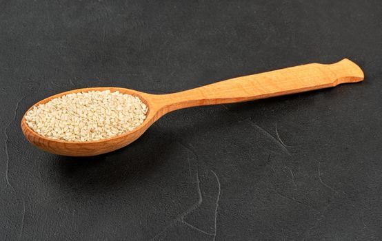 Sesame seeds in a wooden spoon on a concrete background